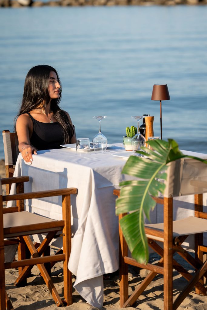 ragazza seduta al tavolo apparecchiato in spiaggia col mare calmo a due passi